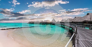 Scenic panoramic landscape view of luxury overwater bungalows at the beach and lagoon during sunset in Moorea, French Polynesia.