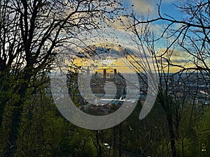 Scenic panoramic view of Lyon skyline at sunrise with silhouetted leafless trees in foreground, modern skyscrapers and historic photo