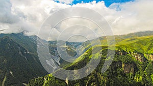 Scenic panoramic view of nature rolling hills landscape with green meadows and mountain peaks in the background with blue clouds