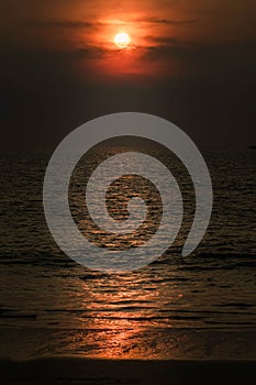 Scenic red orange Sunset with Sun hiding in clouds, glowing light line crosses Sun disk horizontally, vertical orientation photo.