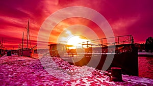 Scenic red purple and violet sunset over countryside river in Europe with old ships having rest at the snowy harbor pier