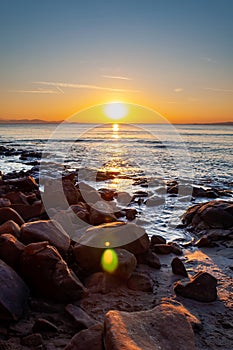 Scenic rocky beach Cala Violina landscape at the sunset. The sun is going down behind the horizon. Tyrrhenian Sea bay at the