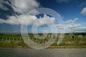 Scenic rural landscape of pastureland with wood posts and wired fence, blue sky and dramatic clouds in Waitomo, New Zealand