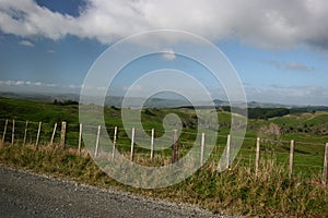 Scenic rural landscape of pastureland with wood posts and wired fence, blue sky and dramatic clouds in Waitomo, New Zealand