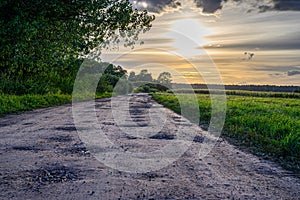 Scenic rural landscape with rural broken dirt road at sunset