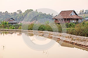 Scenic rural of vietnam at sunset, two old wooden house, brown earthenware roof, pool foreground, forest and mountains backgrounds