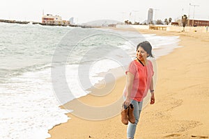 Scenic shot of a Hispanic woman walking on the sand in Barceloneta beach, Barcelona Spain