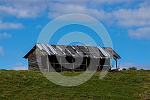 Scenic shot of an old abandoned hut on top of a green hill with a bright blue sky in the background