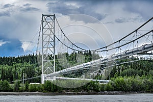 Scenic shot of a pipeline bridge over the Tanana river surrounded by a tall green tree forest photo