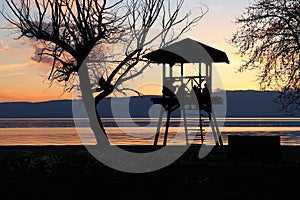 Scenic shot of silhouettes of people in a gazebo on the shore of Lake Ohrid during beautiful sunset