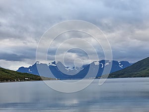 Scenic shot of snowy mountains in distance and a lake reflecting the gloomy clouds