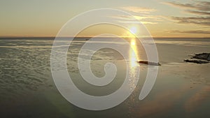 Scenic side high fly over winter sea surface with thin ice floes illuminated by Sunset. Sunlight path on calm sea. Northern Sweden