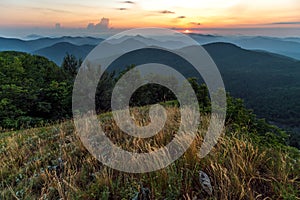 Scenic summer sunset in hazy Caucasus mountains. Sun setting bihind clouds. Beautiful landscape from top of Lysaya mountain in