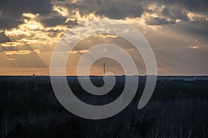 Sunset over the forest with sun rays breaking through clouds