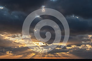 Sunset over the forest with sun rays breaking through clouds