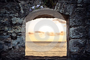 Scenic sunset over sea through window of old ruins with dramatic sky and perspective view with effect of light at the end of tunne