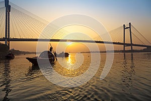 Scenic sunset over Vidyasagar bridge with wooden boats on river Hooghly, Kolkata, India.