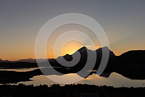 Scenic sunset with sun setting behind two mountains in Lofoten, Norway