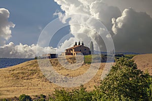 Scenic Tuscan farmhouse in Val d\'Orcia with cypress trees, rolling hills, and distant view of Pienza