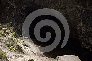 Scenic underground landscape. Shore of an underground lake surrounded by rocks. Darkness in cave corridor and light falling on ban