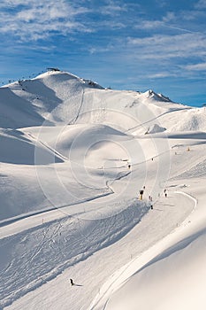 Scenic valley of hilghland alpine mountain winter resort on bright sunny day. Wintersport scene with people enjoy skiing