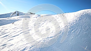 Scenic valley of hilghland alpine mountain winter resort on bright sunny day. Wintersport scene with people enjoy skiing