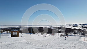 Scenic valley of hilghland alpine mountain winter resort on bright sunny day. Wintersport scene with people enjoy skiing and snowb