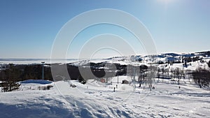 Scenic valley of hilghland alpine mountain winter resort on bright sunny day. Wintersport scene with people enjoy skiing and snowb