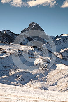 Scenic vertical view of a snowy peak on a sunny day with blue skies and clouds in the background. Unpopulated wild