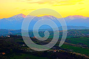 Scenic view from above at hills and mountains under the yellow sunset sky in Monte Vidon Corrado