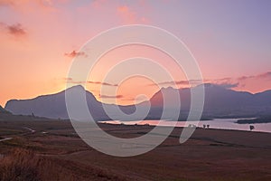 Scenic view of amazing pink-yellow sunset in Sicilian mountains with lake