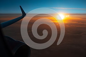 Scenic view of beautiful dark sunrise, cloudy sky and airplane wing with engine, through window of the aircraft during the flight.