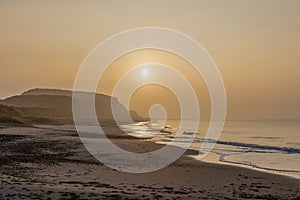 A scenic view of a beautiful sunrise at the beach with some hill in the background