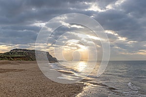 A scenic view of a beautiful sunrise at the beach with some hill in the background and marble sky