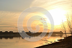 Scenic view of a beautiful sunset over the river in the city in spring against the background of the golden sky, the sun over the