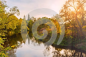 Scenic view of beautiful sunset or sunrise above the pond or river at autumn evening with cloudy sky. Sunbeams pass through the