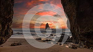 Scenic view of Camilo beach in Algarve featuring the rocky cliffs engulfed by waves at pink sunrise
