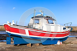 A scenic view of a colorful red, white and blue fishing boat on a Scottish dry dock under a majestic blue sky