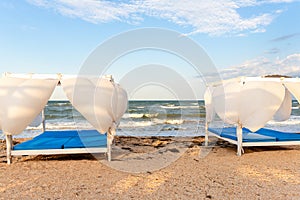 Scenic view empty white beach wooden canopies cabanas with white curtain blowing by wind against stormy sea or ocean san