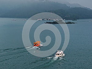 Scenic view of ferries & sightseeing boats navigating on Sun-Moon Lake, a popular tourists destination in Nantou, Taiwan, with mis