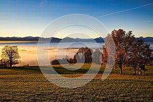 Scenic view of a grassy field with trees and fog, against a backdrop of mountains. Auerberg, Germany photo