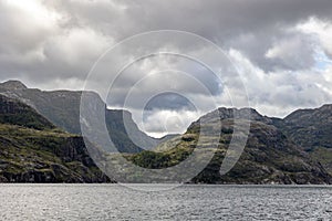 Scenic view of huge rocky mountains in cloudy sky background surrounded by the lake