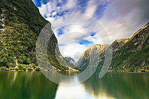 Scenic view of huge rocky mountains in cloudy sky background surrounded by the lake