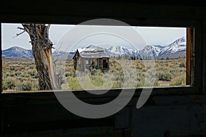 Scenic view of a hut in the arid wild through the window of a decaying house.