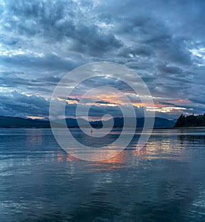 Scenic view of a lake with mountains in the distance and a yellow sunset hiding behind clouds