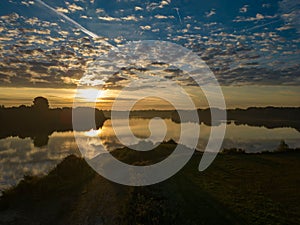 Scenic view of a lake reflecting green trees on its shore and a beautiful cloudy sky at sunset