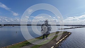 Scenic view of a large metal sculpture by a calm lake with a clear blue sky overhead, featuring a boat sailing in the distance and