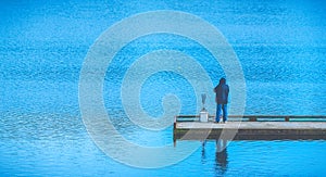 Scenic view of a man fishing on a pier in a big lake in the park.