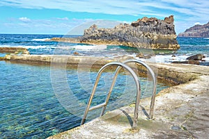 Scenic view of a metal ladder leading into a clear sea water pool with the Atlantic behind.