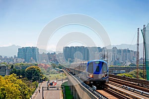Scenic view of a metro train traveling on elevated rails of Taoyuan Airport MRT System and residential buildings clustering in bac